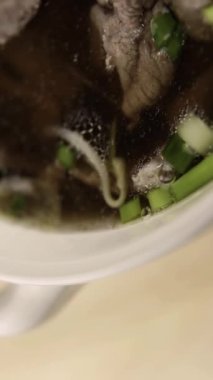 Pho bo. Beyaz bir kasede Vietnamlı pho bo çorbası. Yeşil soğan, sığır eti. Dikey video. Dikey.