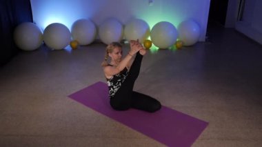 Janu Sirsasana. Tepeden tırnağa ileri eğil. Krounchasana. Heron Pozu. Esnek, orta yaşlı bir sarışın fitness kulübünde yoga yapıyor. Paspasın üstünde Asya yogası yapıyor..