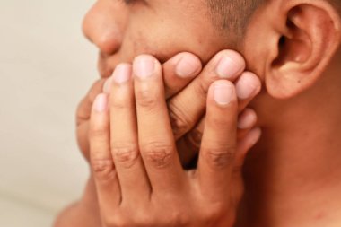 Elleriyle ağzını kapatan bir adamın beyaz bir arka planla yakın plan fotoğrafını çek.