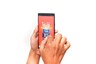 Güney Lampung, 14 Aralık 2025: '12' ile canlı turuncu ekranı gösteren cep telefonuyla ellerinizi kapatın