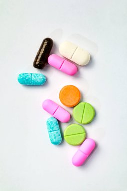 Çeşitli renkli hap kapsülleri yumuşak stüdyoda temiz beyaz bir yüzeye dağılmış durumda.