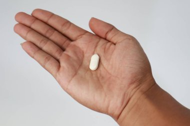 Tek bir beyaz oval hapın, bir insanın avucunun içinde, temiz bir insanın eline karşı tutulan görüntüsünü yakından takip et.