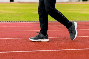 Siyah atletizm pantolonu ve kırmızı bir pistte yürüyen koşu ayakkabısı giymiş birinin bacakları yakın plan görüntüsü..