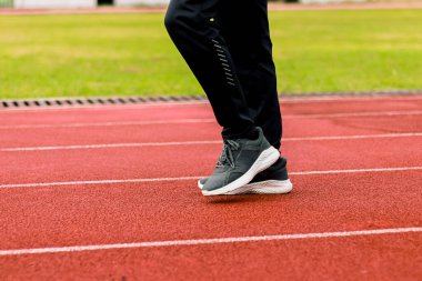 Kırmızı koşu pistinde spor ayakkabıları ve siyah spor pantolonları giyen birinin bacakları ve ayaklarının yakın plan görüntüsü..