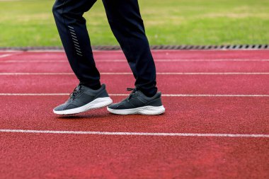 Kırmızı bir atletizm pistinde ayak ve bacakların yeşil çimlerle çevrili olduğu yakın plan bir fotoğraf..