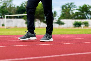 Kırmızı koşu pistinde spor ayakkabısı ve pantolon giyen birinin bacaklarının yakın çekimi, egzersiz için hazır..