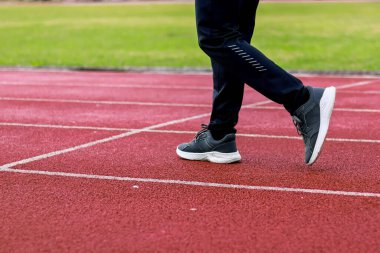 Bir insanın bacaklarının ve atletik ayakkabılarının beyaz şeritli kırmızı bir pistte yürüme görüntüsü..