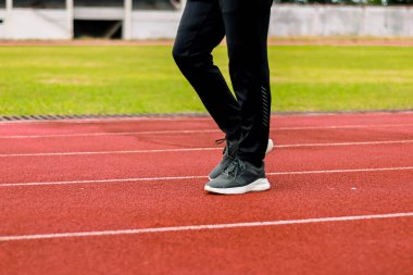 Kırmızı pist üzerinde spor pantolonları ve koşu ayakkabıları giyen birinin bacaklarının yakın çekimi..