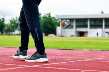 Bir stadyumdaki kırmızı sentetik koşu pistinde yürürken bir insanın bacaklarını ve ayaklarını kapatın..