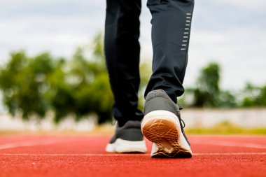 Kırmızı koşu yolunda yürüyen bir insanın bacakları ve ayaklarının yakın görüntüsü.