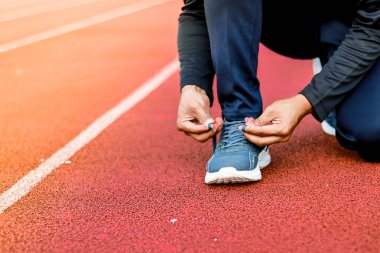 Canlı kırmızı bir atletizm pistinde, ayakkabı bağcıklarını koşu ayakkabısına bağlayan birinin ellerine yakın plan..