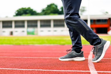 Kırmızı bir atletizm pistinde yürüyen, siyah pantolon giyen ve koşu ayakkabısı giyen birinin bacaklarının yakın çekimi..