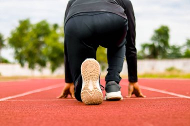 Başlangıç bloklarında bir atletin yakın plan dikiz görüntüsü, odaklanmış ve bir stadyum pistinde yarışa başlamaya hazır..