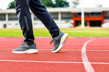 Kırmızı bir atletizm pistinde koyu renk eşofman ve koşu ayakkabılarıyla bir sporcunun bacaklarının yakın görüntüsü..