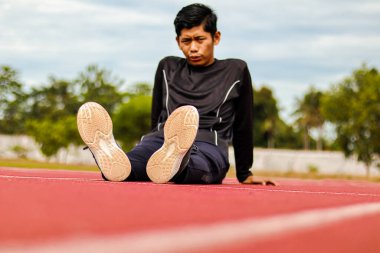 Genç erkek sporcu kırmızı bir pistte dinleniyor, yoğun fiziksel antrenmandan sonra yorgun görünüyor..