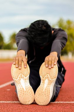 Atlet kırmızı bir pistte bacak esnekliğine odaklanarak viraj hareketi yapıyor..
