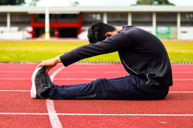 Atletik giysili bir insan, canlı kırmızı koşu pistinde dizlerinin üstüne çökerek dans eder..