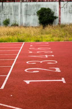 Beyaz şerit numaraları ve çizgileri olan kırmızı koşu yolu, açık hava manzarasını gösteriyor.