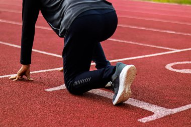 Kırmızı koşu pistinde başlangıç pozisyonunda bir sporcunun yakın çekimi, yarışa hazırlanıyor..