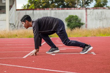 Sentetik koşu pistinde düşük başlangıç pozisyonunda odaklanmış genç bir atlet yarışa hazırlanıyor..