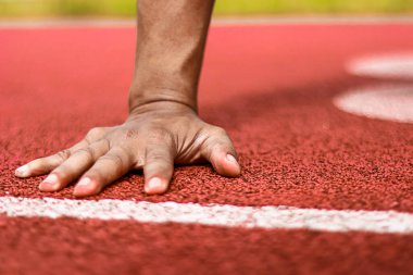 Kırmızı koşu pistinin başlangıç çizgisinde dinlenen bir sporcunun eli, yarışa hazırlanıyor..