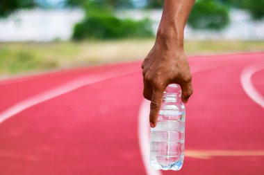 Canlı kırmızı koşu pistinde elinde temiz bir su şişesi tutan bir sporcunun yakın çekimi..