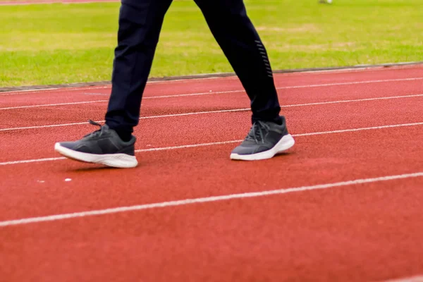 Kırmızı sentetik koşu pistinde yürüyen bir insanın bacak ve ayaklarının yakın plan görüntüsü..