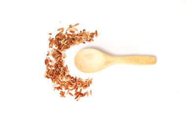 İşlenmemiş kahverengi pirinç taneleri, temiz beyaz bir yüzey üzerinde küçük bir tahta kaşığın yanında serpilmiş..