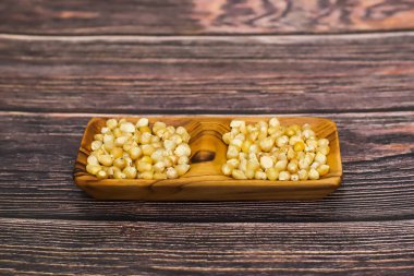 Kırsal bir ahşap yüzey üzerinde ahşap bir kapta pişmemiş mısır tanelerinin iki küçük porsiyonu..