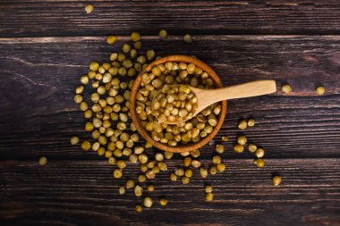 Kurumuş mısır tanelerinin tepeden görünüşü ahşap bir kaseden siyah bir ahşap yüzeye dökülüyor, tahta bir kaşıkla..