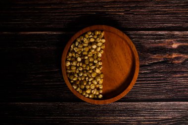 Pişmemiş mısır çekirdekleri, koyu ahşap bir yüzey üzerine sade ahşap bir kasede dizilmiş..