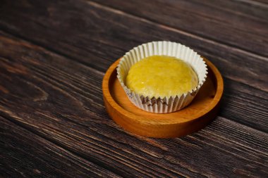 Tek, yuvarlak, altın renkli mochi tatlısı beyaz kağıt bir kalemde sunuluyor, kırsal ahşap bir yüzeyde dinleniyor..