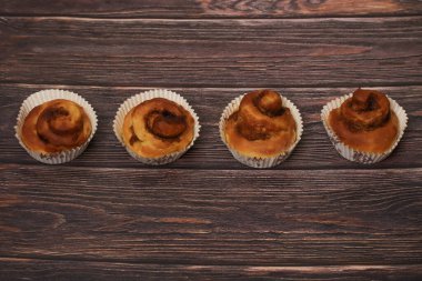 Koyu, ahşap bir arka planda kağıt bardaklarda servis edilen dört lezzetli tarçınlı hamur işi..