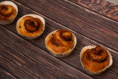 Kırsal ahşap bir yüzeye dizilmiş dört yeni pişmiş tarçın rulosu..