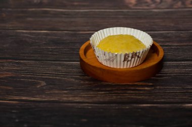 Dekoratif kağıtta servis edilen yalnız bir kek, ahşap bir yüzeye karşı dizilmiş küçük bir ahşap tabakta duruyor..