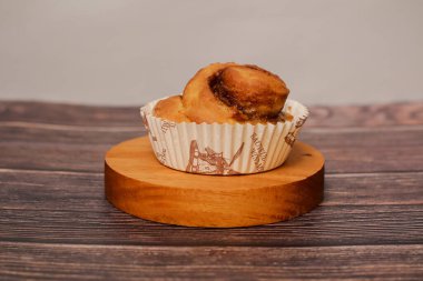 Tek, taze pişmiş tarçınlı pasta dekoratif bir kağıt kaplamasında servis edilir, kırsal ahşap bir stantta sunulur..