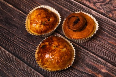 Üç tane yeni pişmiş tatlı hamur işi, içinde iki kek ve ahşap bir yüzeye yerleştirilmiş tarçınlı rulo..