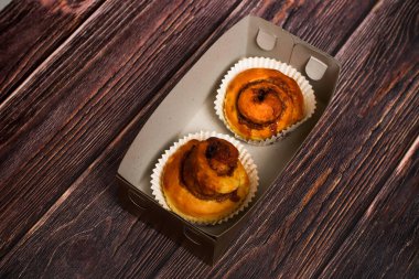 Kağıt kaplamalı lezzetli tarçınlı hamur işleri. Koyu ahşap bir yüzeyde basit bir karton kapta sunuluyor..