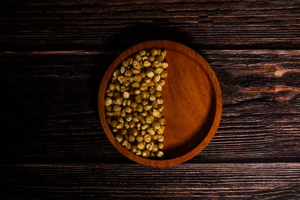 Pişmemiş mısır çekirdekleri, koyu ahşap bir yüzey üzerine sade ahşap bir kasede dizilmiş..