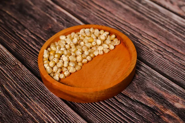 Kurumuş mısır taneleriyle dolu ahşap bir kase desenli ahşap bir yüzey üzerinde duruyor..