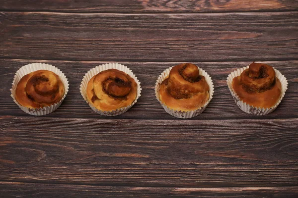 Koyu, ahşap bir arka planda kağıt bardaklarda servis edilen dört lezzetli tarçınlı hamur işi..