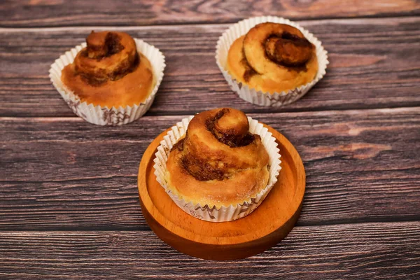 Üç lezzetli tarçınlı rulo beyaz kağıt kaplamalı, kırsal ahşap bir yüzey üzerinde, biri küçük ahşap bir tabakta..