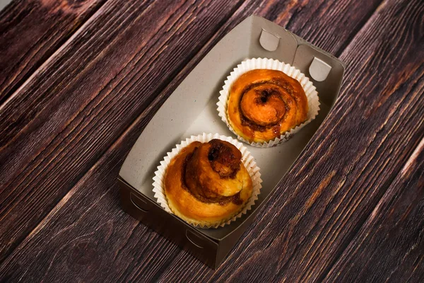 Kağıt kaplamalı lezzetli tarçınlı hamur işleri. Koyu ahşap bir yüzeyde basit bir karton kapta sunuluyor..