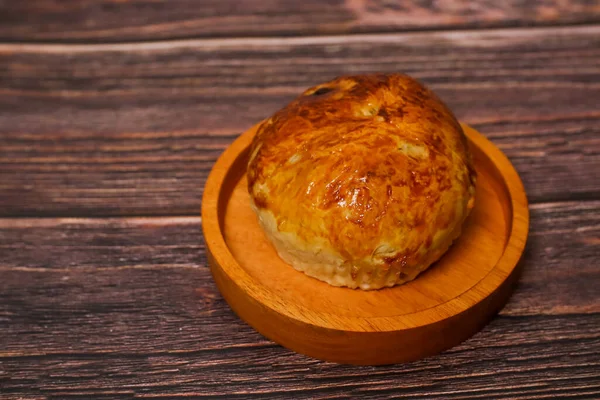 Kaba ahşap bir yüzeye karşı küçük bir ahşap tabakta duran tek bir altın-kahverengi hamur işi..