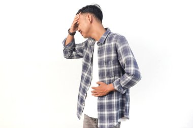 Asyalı bir adam ekose bir gömlek giyiyor ve kederli bir ifadeyle başını ve karnını beyaz üzerinde tutuyor..