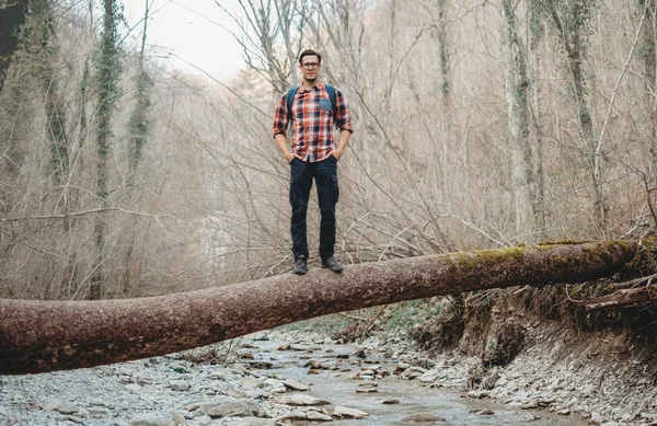 Uomo escursionista sul tronco d'albero sul fiume — Foto Stock