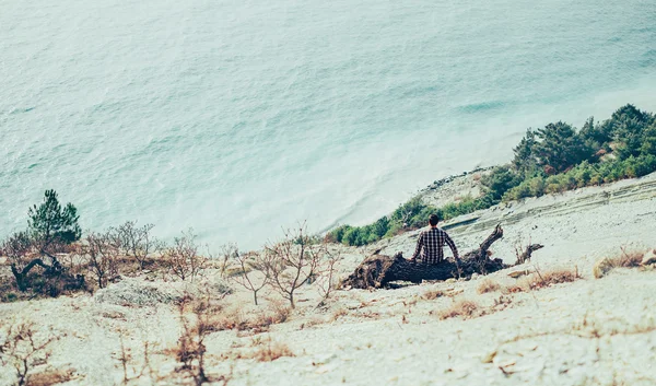 Man sitting on snag on coastline — Stock Photo, Image