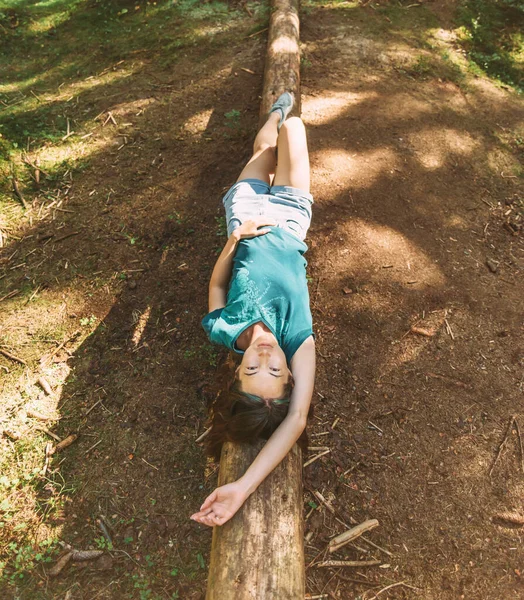 美丽的年轻女子躺在倒下的树干上悠闲自在地望着夏日森林里的相机 — 图库照片