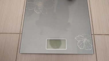 Çıplak ayaklı genç bir kadın elektronik teraziye basıyor ve ağırlığını ölçüyor..