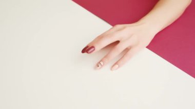 Modaya uygun manikürlü genç bir kadın eli pembe ve beyaz renkli masaya parmağını vuruyor. Endişe, stres, bekleme kavramı. 
